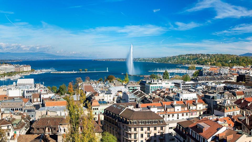 Panorama urbano de Ginebra con una vista aérea de la fuente Jet d'eau, el lago Leman, la bahía y el puerto desde el campanario de la catedral de Saint-Pierre. Día soleado y cielo azul.