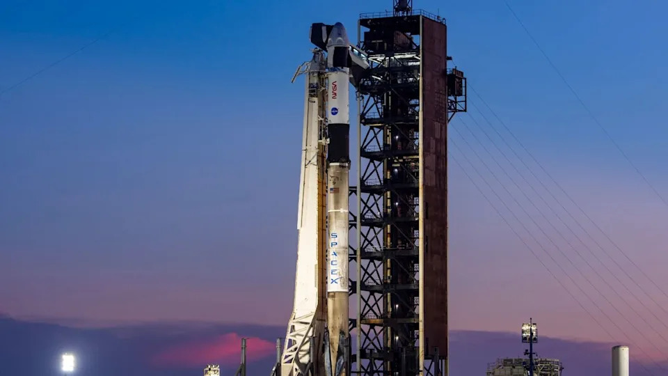  A white rocket stands upright on a launch pad at sunset. 