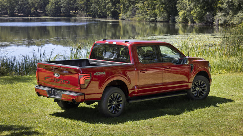 A red Ford F-150 pickup truck in rear three-quarter view in front of a lake