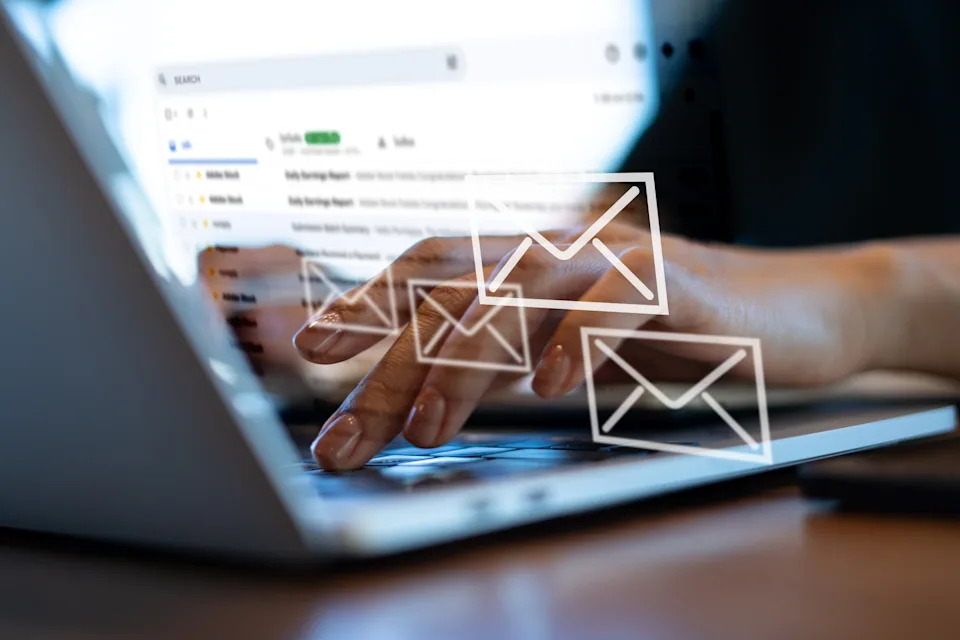 Hands typing on a laptop with email icons overlay, illustrating email communication in a work setting