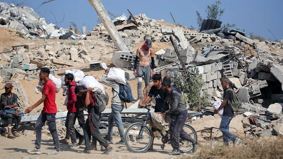 Palestinians carry sacks of aid past rubble