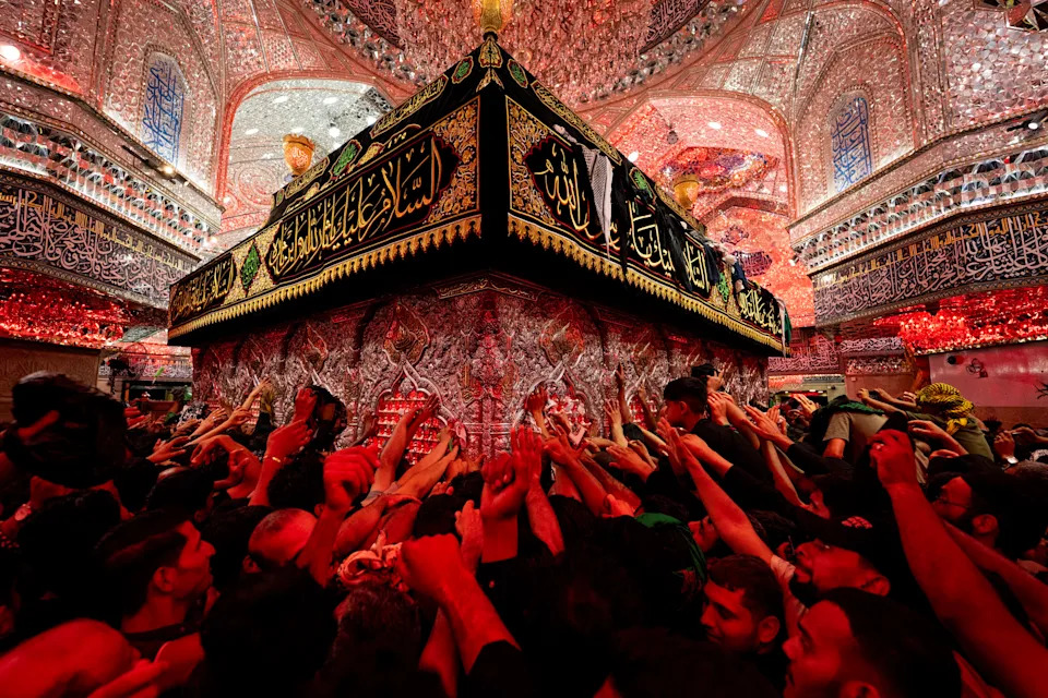 Many worshipers in a shrine reach out to touch a tomb.