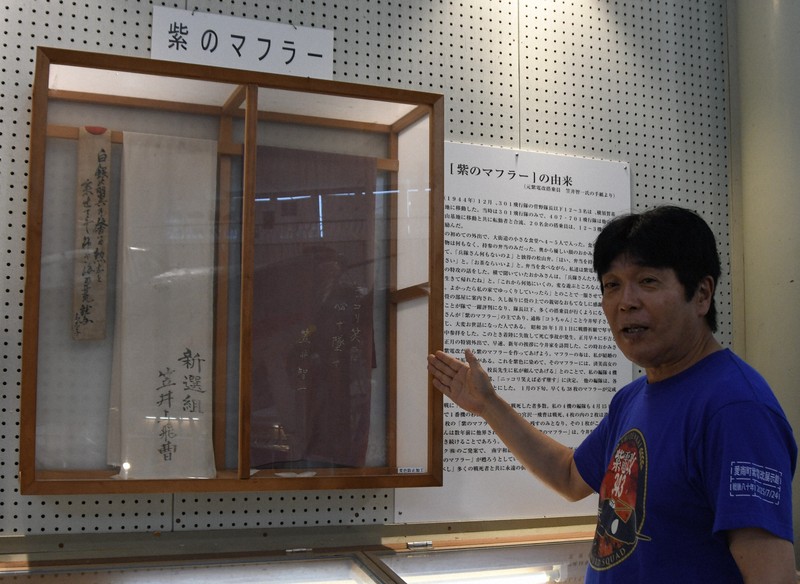 紫電改展示館には、笠井智一さんから寄贈された紫のマフラーが展示されている。紹介するのは永元一広館長＝愛媛県愛南町で2025年8月9日午後2時30分、狩野樹理撮影