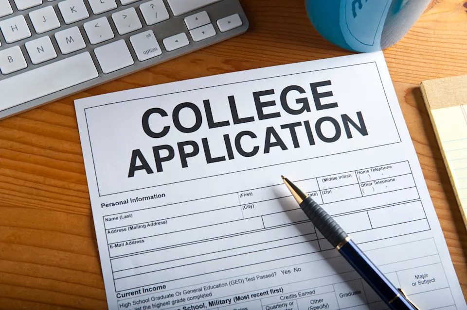 College application form on a desk with a pen, partially filled near a keyboard