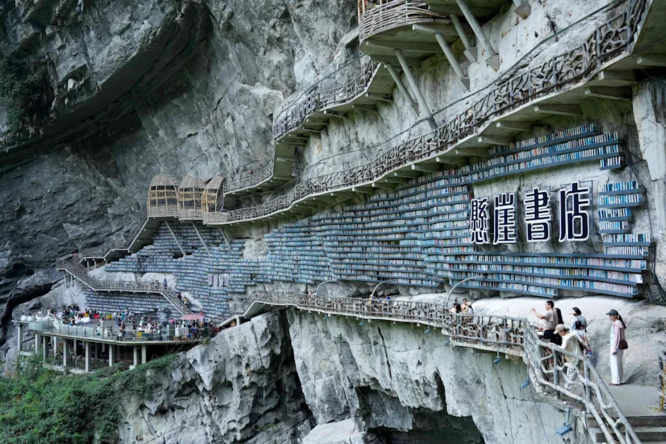 Long walkways are built onto the side of a steep rock cliff, which is lined with many rows of bookshelves.