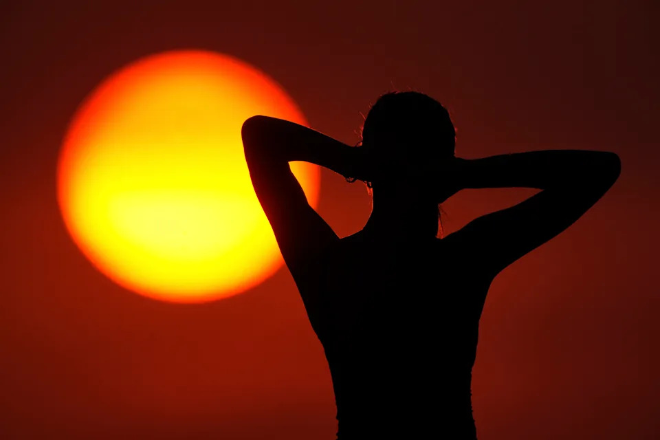 A person stands silhouette in front of the sun.