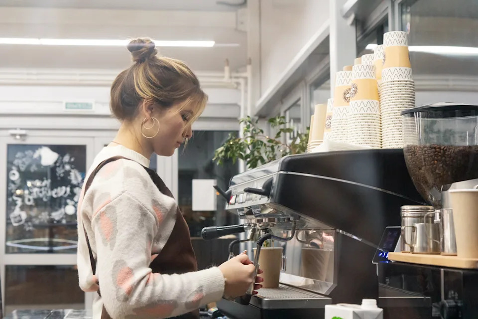 Barista making coffee in a café, focused on brewing, with stacks of cups visible