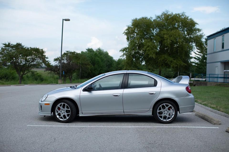 side view of silver sedan parked in lot beside grassy area and trees.