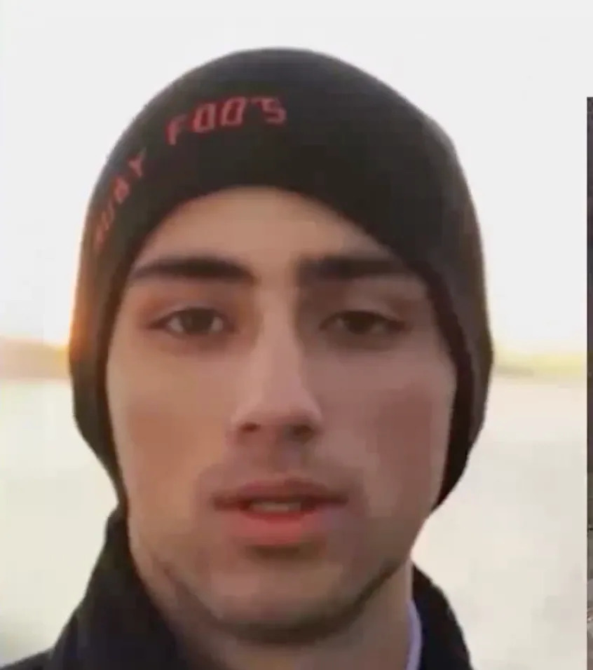 Person wearing a beanie with embroidered text. Background appears outdoors, and the expression is neutral