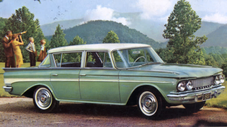 An old picture of a 1961 Rambler American parked outdoors with a family of four in the background.