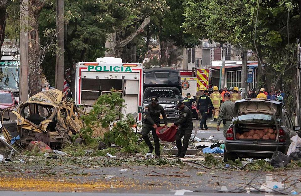 Varios policías cargan un cuerpo en unas mantas y caminan entre escombros luego de la explosión en Cali, Colombia.