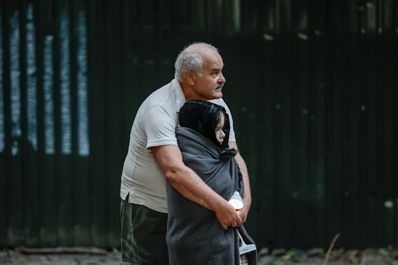 A man embraces a child as they stand at the site of buildings hit by Russian missile and drone strikes on Kyiv, Ukraine on August 28, 2025. / Credit: Alina Smutko / REUTERS