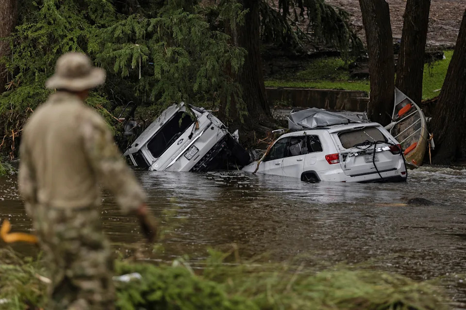 a man walks by two submerged vehicles piled in flood waters