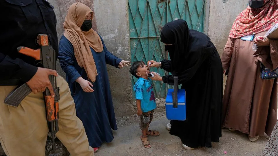 A police officer stands guard while a health worker, center, administers a polio vaccine to a child in Karachi, Pakistan, in April. - Fareed Khan/AP