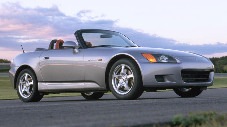 A Honda s2000 parked on a pave stretch of road during a sunset