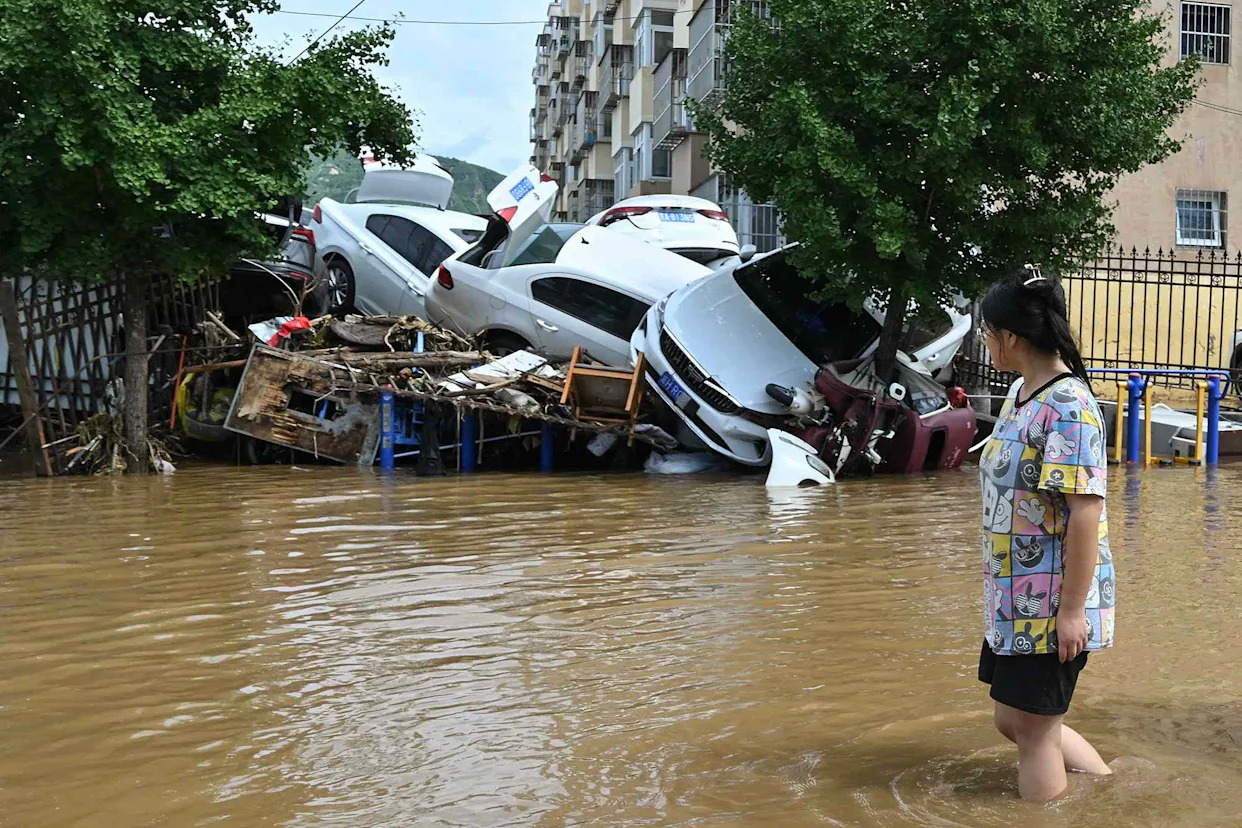 ADEK BERRY/AFP via Getty A woman walks past damaged cars in a flooded neighbourhood in Miyun district, China, on July 29