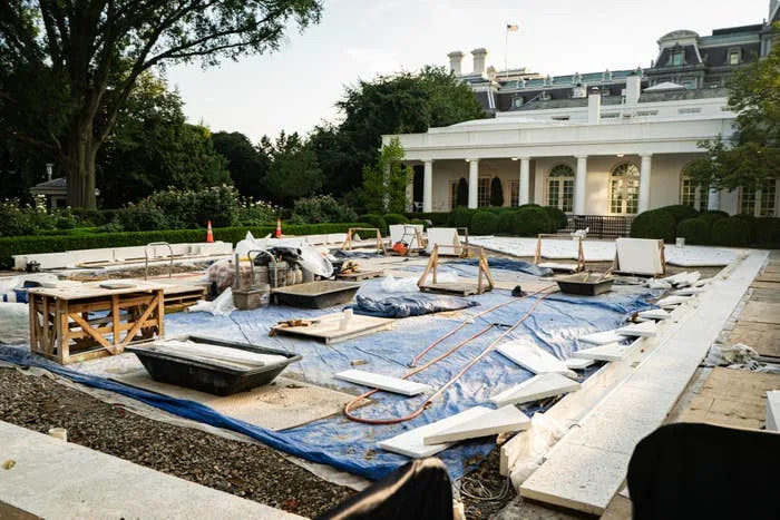 Rose Garden under renovation with construction materials, tools, and tarps scattered. White building with arched windows in the background