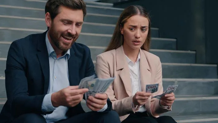 Two people in business attire sitting on stairs, counting money. One appears happy, the other looks worried
