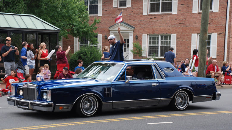 A blue early '80s Ford Thunderbird that's bagged and riding low in a parade