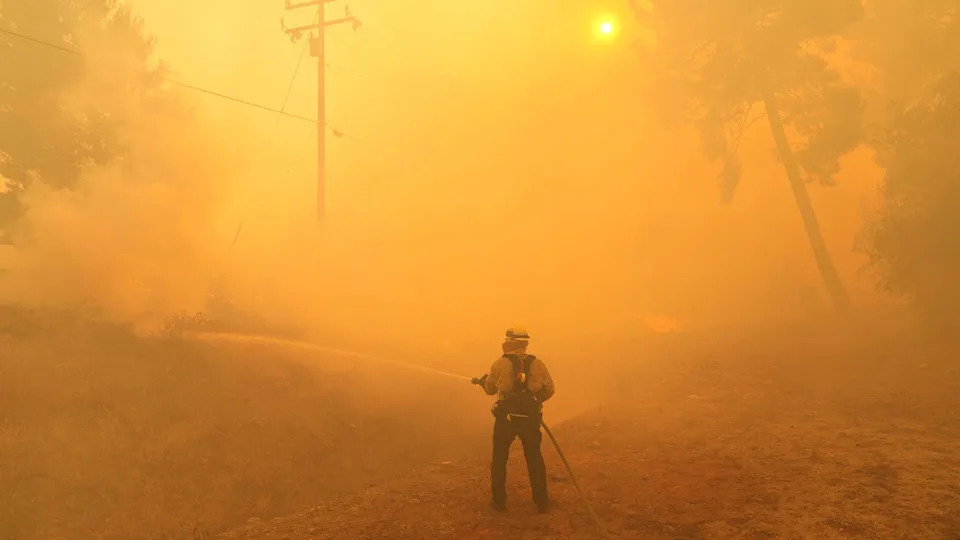 A firefighter stands in thick smoke with the sun shrouded in front of them