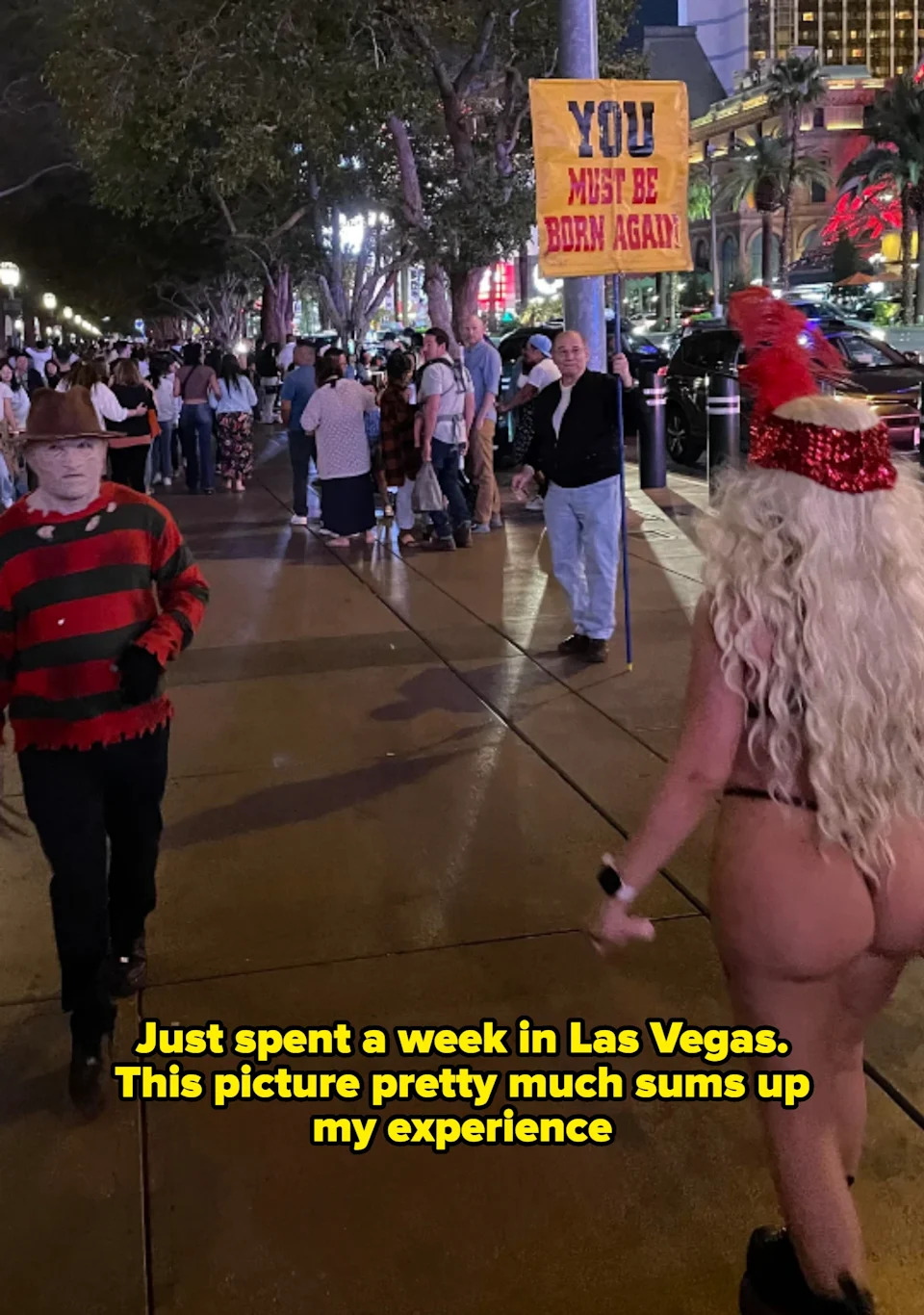 Person dressed as Freddy Krueger walks past a performer in revealing attire. A man holds a sign saying "YOU MUST BE BORN AGAIN" in the background. Caption: "Just spent a week in Las Vegas. This picture pretty much sums up my experience"
