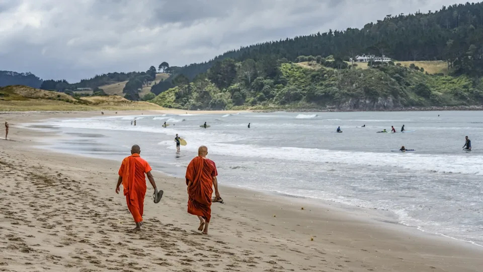 Buddhist Monks walking on the sand of Hot Water Beach. An underground river of hot water flows from the interior of the earth to surface in the Pacific Ocean at Hot Water Beach, North Island. Waikato Region, New Zealand. (Photo by: Keith Levit/Design Pics Editorial/Universal Images Group via Getty Images)