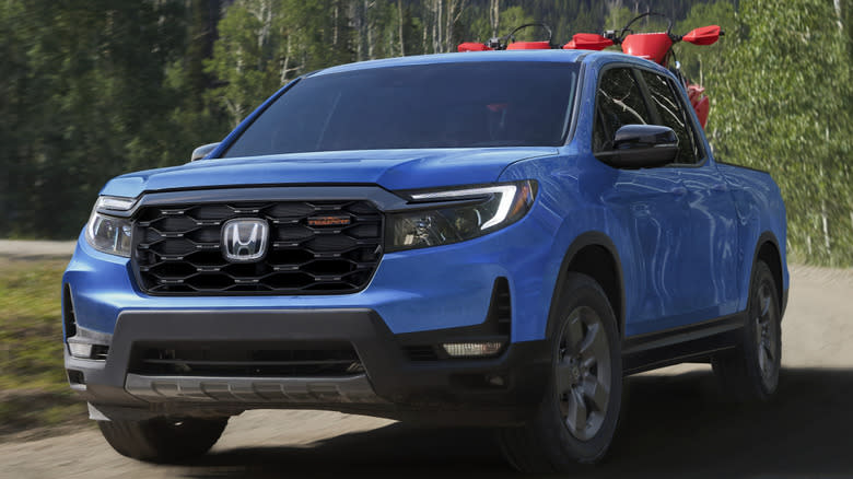 A diffused sky-blue pearl Honda Ridgeline TrailSport driving on a wooded road