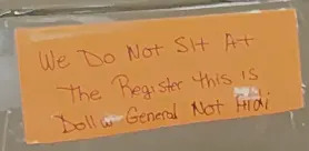 Handwritten sign on a chair stating 'We Do Not Sit At The Register This Is Dollar General Not Aldi' indicating seating not allowed