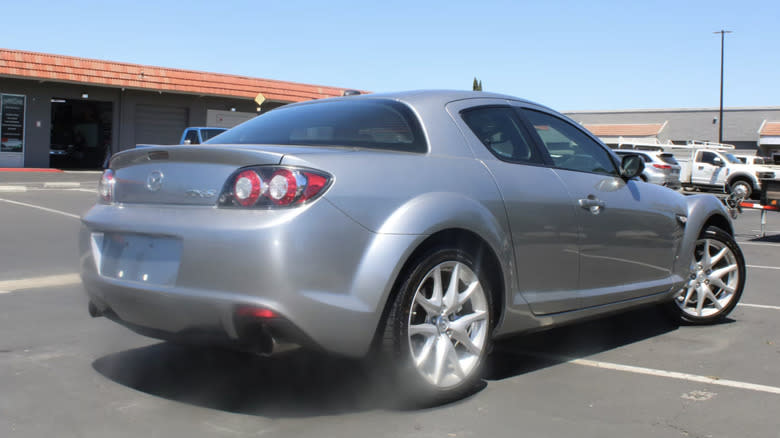 A blurry picture of a silver 2011 Mazda RX-8 Grand Touring Coupe in a strip mall parking lot