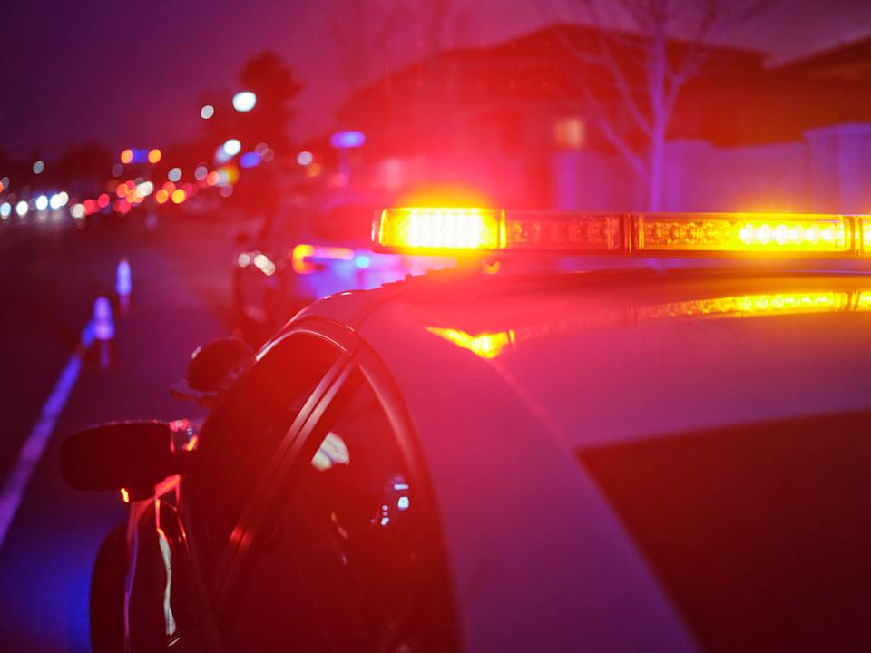 A police car at night alongside a road with emergency lights flashingGetty