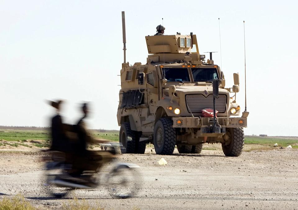 Afganos conduciendo una motocicleta junto a un Army Mine Resistant Ambush Protected (MRAP) del 508º Batallón de Tropas Especiales, 82ª División Aerotransportada del Ejército de Estados Unidos, en un puesto de control de la policía afgana en la Autopista Uno, la principal carretera del país, a las afueras de la ciudad de Kandahar, en el sur de Afganistán, el 25 de marzo de 2010.