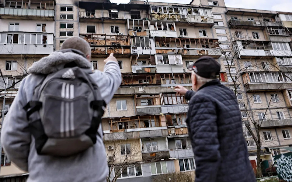 Men stand and look at a damaged high-rise apartment building after a Russian drone strike on March 23, 2025 in Kyiv, Ukraine