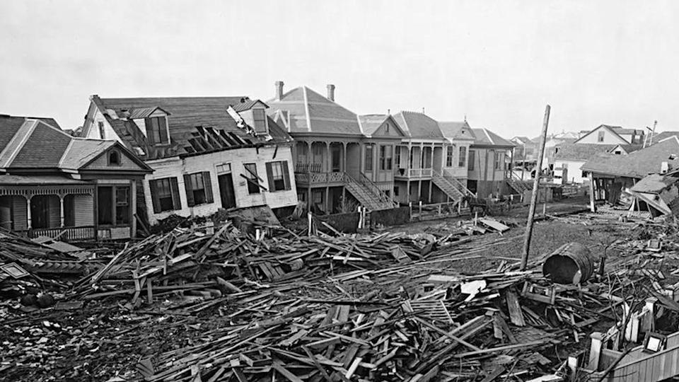 Una foto en blanco y negro muestra la destrucción ocasionada por el huracán de Galveston. Se ven varias casas destruidas y escombros.