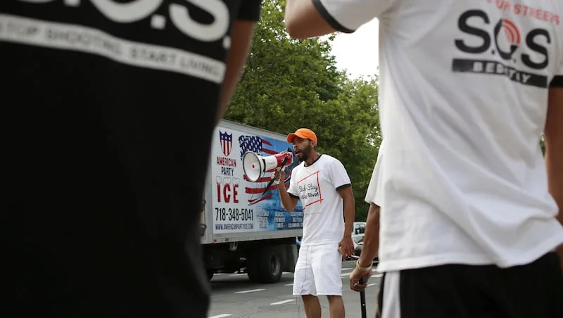 In this July 24, 2018, photo, David Gaskin uses a megaphone during a shooting response in the Brooklyn borough of New York. S.O.S. is one of a growing number of taxpayer-financed &#x00201c;violence interrupter&#x00201d; groups in the nation&#x002019;s largest city that enlist former gang members to attack acts of violence like outbreaks of a disease that they must keep from spreading.