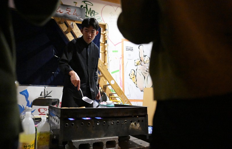 鉄板を使ってバンパロタを揚げ焼きにする藤田昂太郎さん。藤田さんの前には、炊き出しをもらうための寮生らの列ができていた=京都市左京区で2025年5月17日、山崎一輝撮影