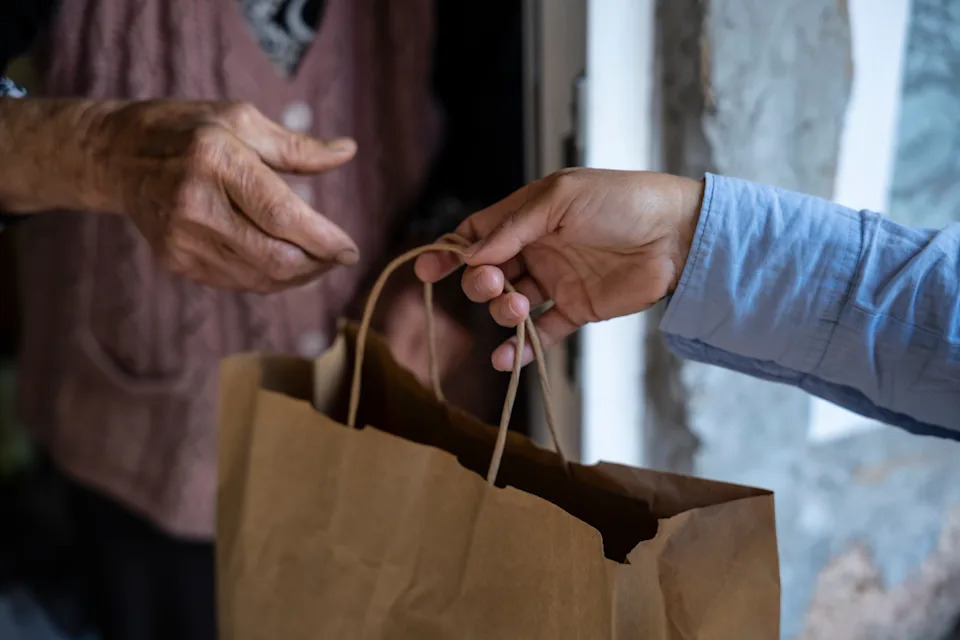 One person hands a paper bag to another at a doorway, symbolizing delivery or service exchange