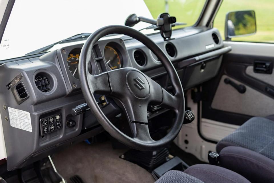 interior view from driver side seat showing three spoke steering wheel, analog gauges, and manual gear shifter.