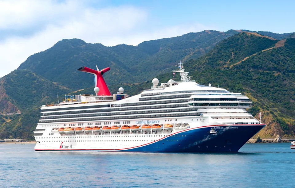 General views of the Carnival Radiance cruise ship at Avalon harbor with mountains and cloudy, blue skies in the background.