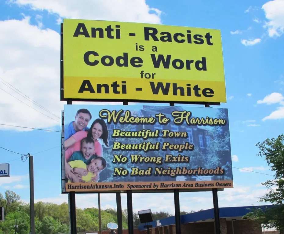 Billboard reading "anti-racist is a code word for anti-white" and a town welcome sign highlighting attributes of Harrison like "beautiful people" and "no bad neighborhoods"
