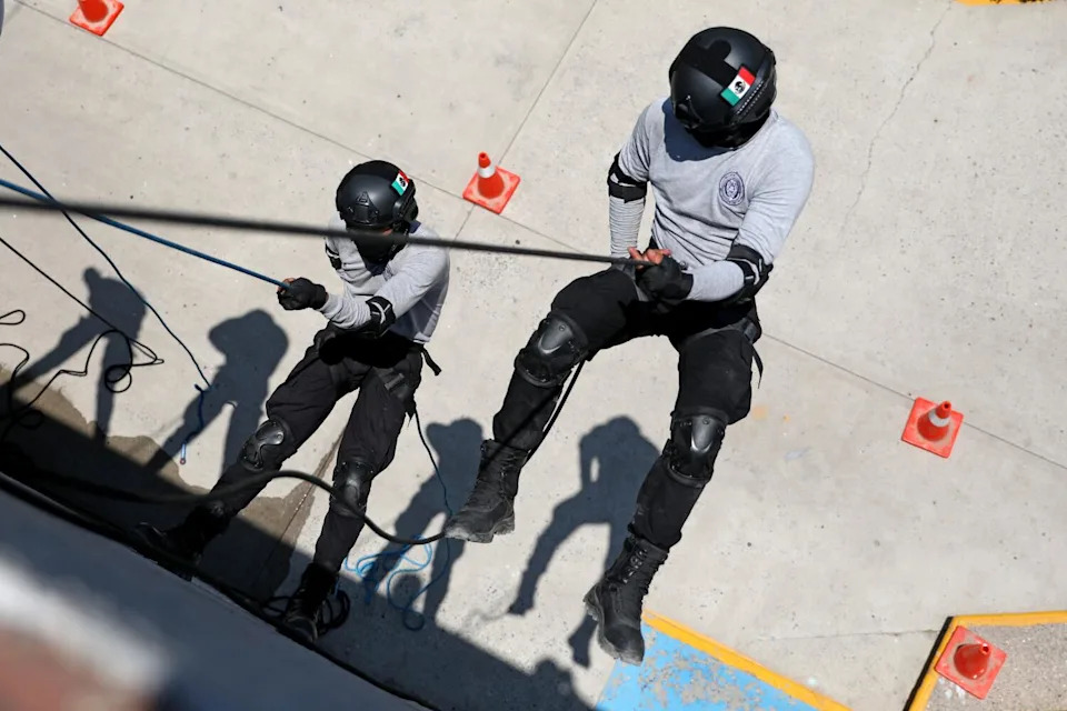 Cadets in helmets rappel down a building.