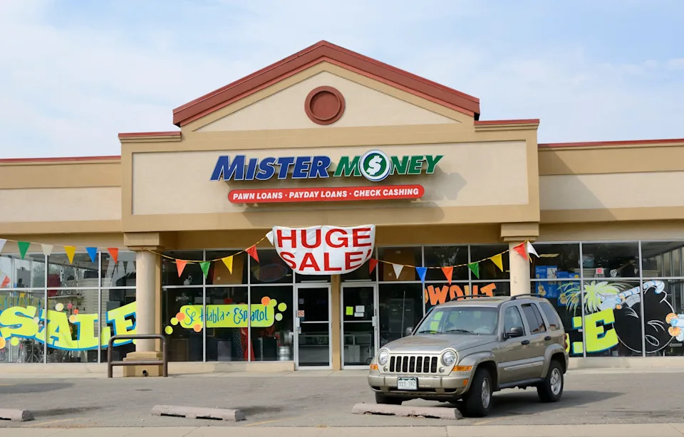 Storefront of Mister Money offering pawns, payday loans, and check cashing, displaying a "Huge Sale" banner and colorful advertising signs