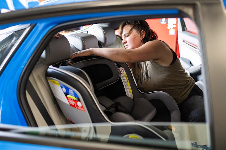 a photograph of a person installing a convertible car seat in the back of a blue sedan