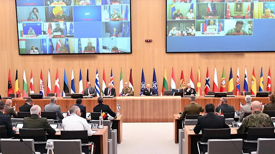 NATO defense chiefs meet in Brussels with large monitors displaying virtual participants from allied nations