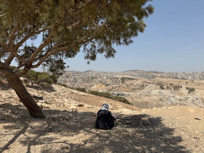 En la foto aparece Abu Emad de espaldas, a la sombra de un árbol, vestido con un traje tradicional negro y con una kufiya palestina en la cabeza, mientras mira hacia Jerusalén.