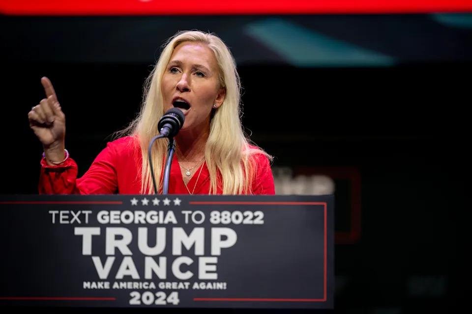 Person speaking at a podium with a political sign displaying a call to action for Georgia voters related to Trump and Vance in 2024
