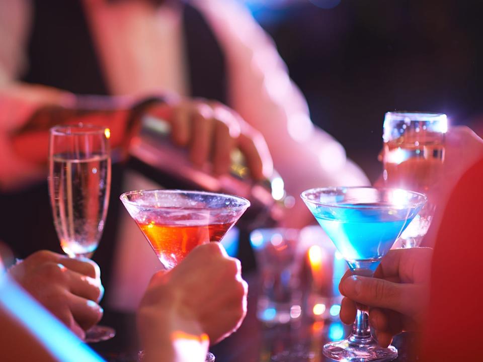 Hands holding cocktails at a bar.