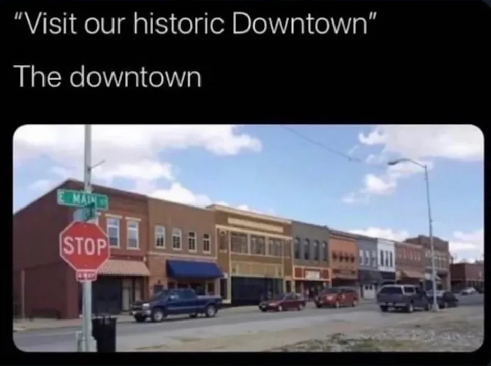 Image showing a small, quiet street with a row of simple buildings and a stop sign. Text jokes about it being an "historic Downtown."