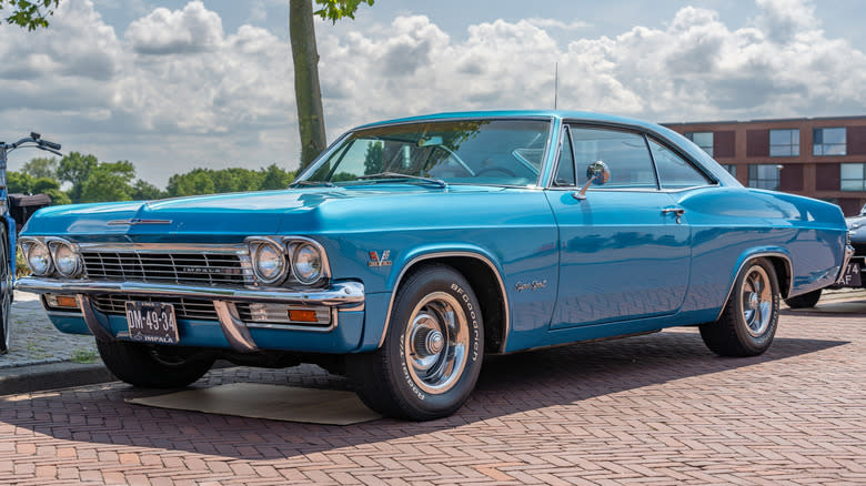 A blue 1965 Chevy Impala parked on a brick street.