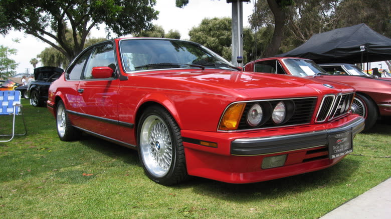 A red 1987 BMW M6 parked on grass at a car show