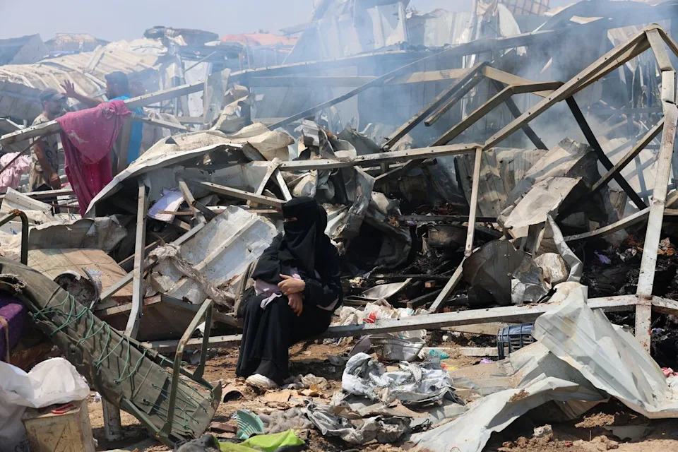A woman sits amid wreckage as Palestinians inspect the damage at the site of an Israeli strike on a tent camp sheltering displaced people, in Deir Al-Balah, in the central Gaza Strip, August 21, 2025. REUTERS/Ramadan Abed